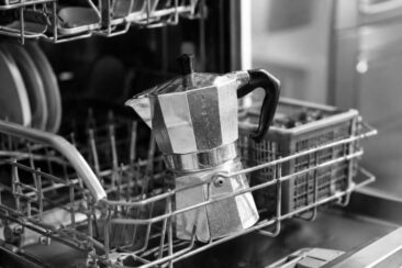 A black and white image featuring a dishwasher and a coffee pot, showcasing a simple kitchen scene with essential appliances.